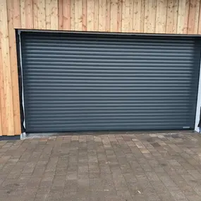 Modernes Garagentor aus Aluminium mit Holzfassade und gepflasterter Einfahrt.