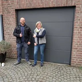 Zwei Personen stehen lächelnd vor einem modernen, grauen Garagentor aus Aluminium.