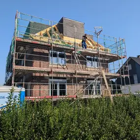 Ein neues Einfamilienhaus mit Gerüst wird bei sonnigem Wetter gebaut, Dacharbeiten laufen.