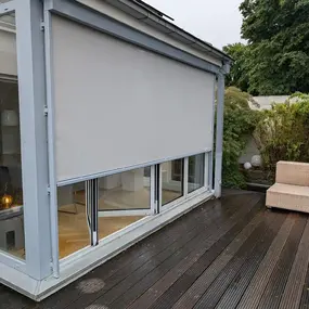 Moderner Sichtschutz als Außenrollo an Wintergarten auf Holzterrasse mit Gartenmöbel.