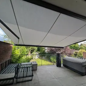 Große Terrasse mit moderner Markise, Gartenblick, Sitzmöbeln und Grill in Wohngebiet.