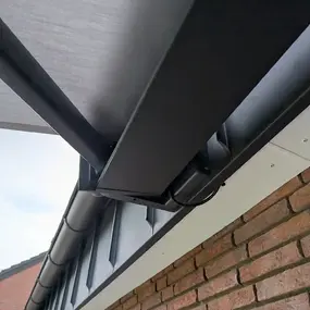 Moderne elektrische Markise an einer Hausfassade mit Ziegelmauer und Dachrinne montiert.